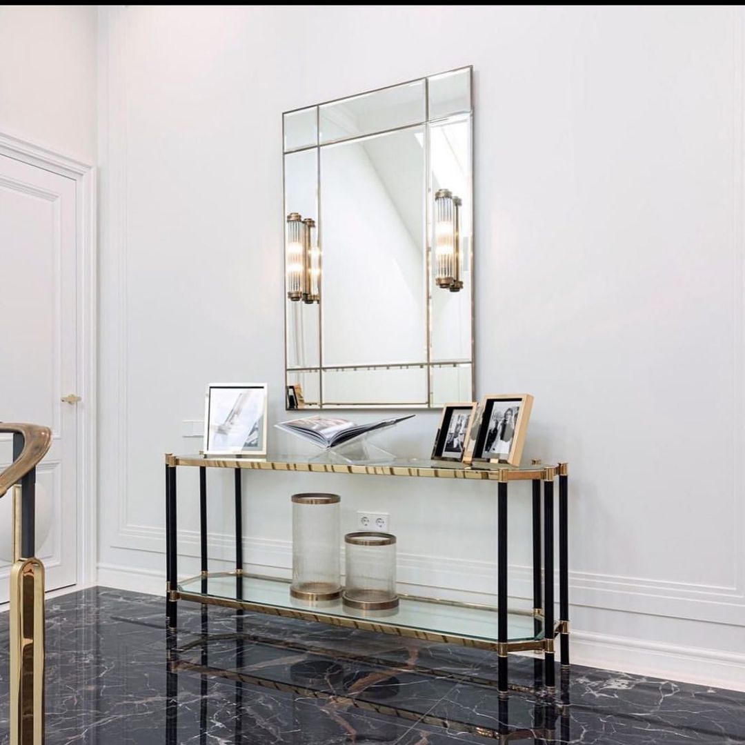 Marble wall console with black base under an elegant wall mirror with lights.